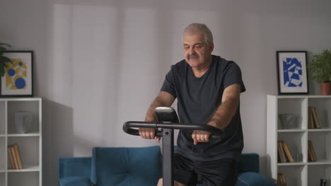 portrait-of-middle-aged-man-on-stationary-bike-in-apartment-training-at-home-cardio-workout-for-keeping-good-physical-condition